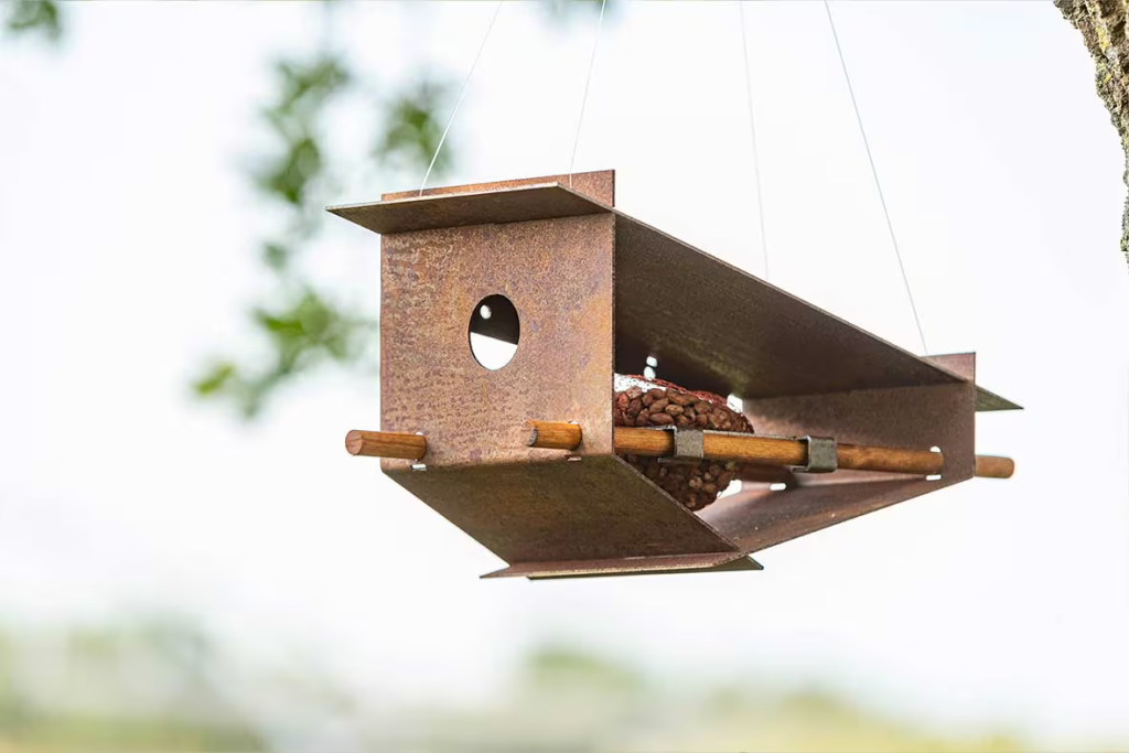 Stalen vogelhuisje aan een tak met groen op de achtergrond