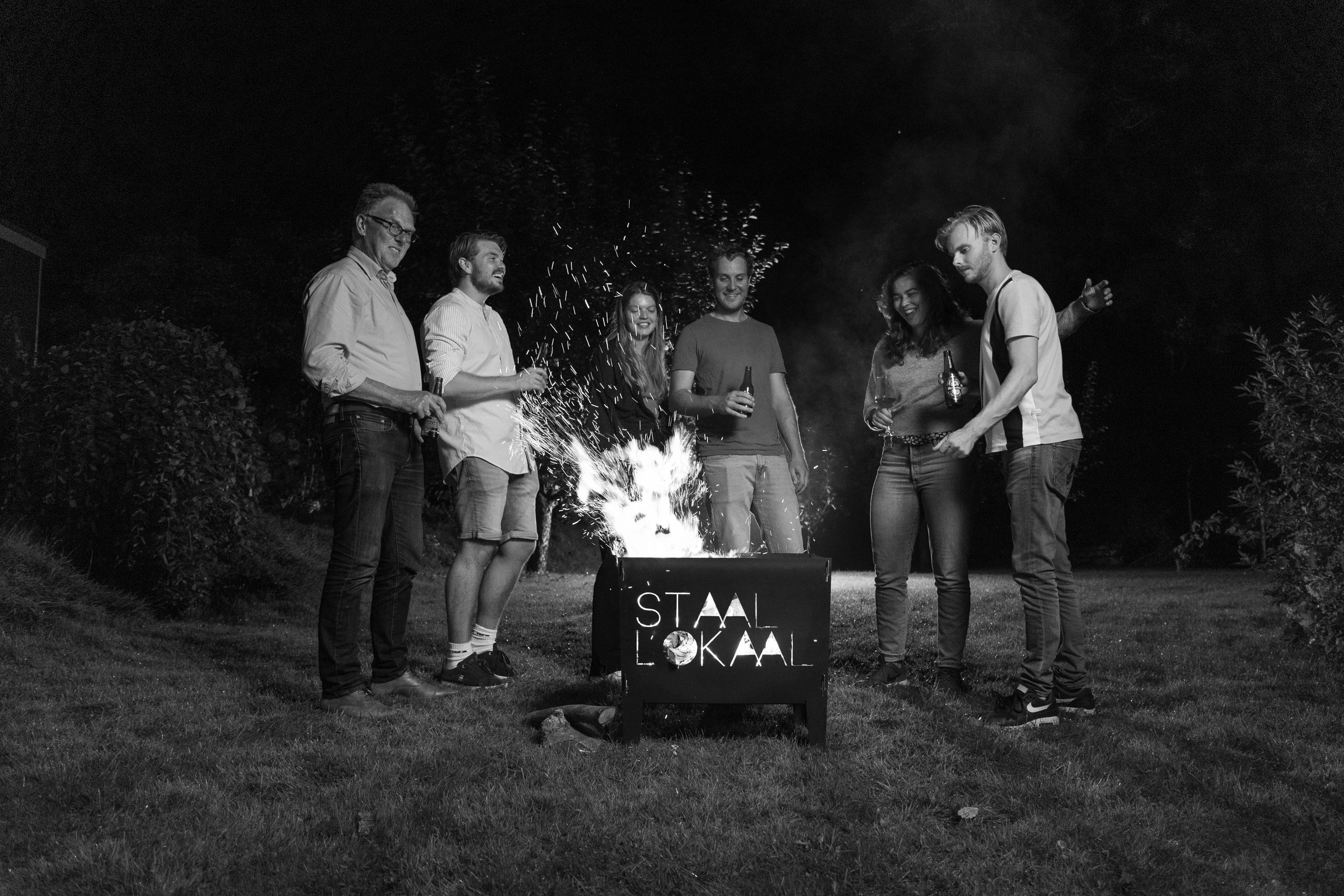 Collega's staan 's avonds samen rond een brandende stalen vuurkorf