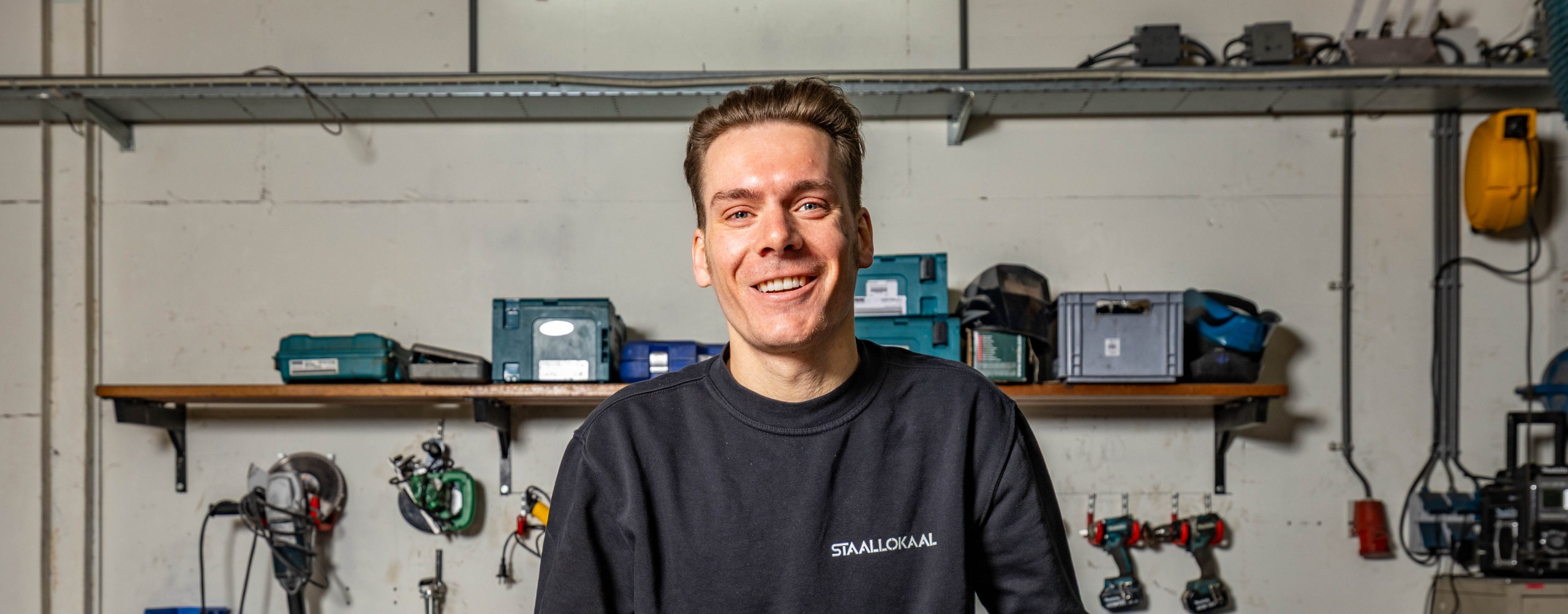 Offerte aanvragen bij Robert van Lokaalverrast, lachend in de werkplaats met gereedschap aan de wand